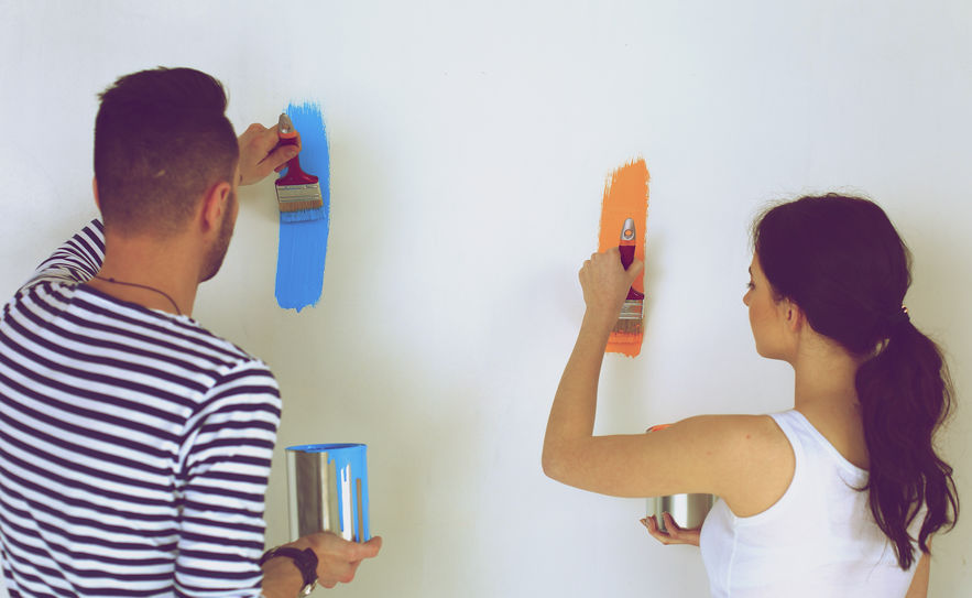 Portrait of happy smiling young couple painting interior wall of new house.