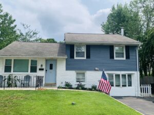 A split-level house with blue and white exterior, a front lawn, and an American flag near the driveway.