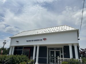 A Bank of America branch building with a white roof, columns, and clear signage under a partly cloudy sky.