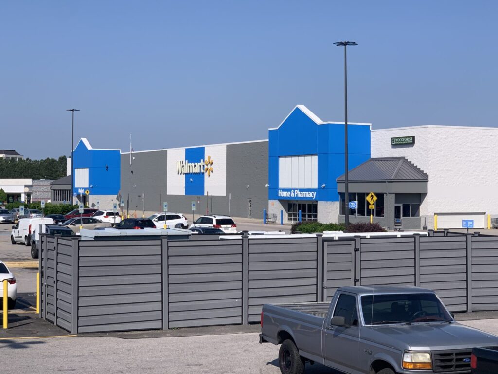 Walmart storefront and parking lot with several parked vehicles on a clear day.