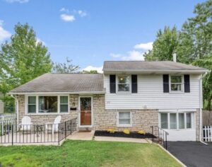 Split-level house with stone and siding exterior, black shutters, front porch, and a paved driveway, surrounded by trees.