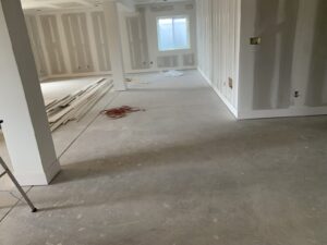 A room under construction with unfinished drywall, scattered wood planks, and a window in the background.