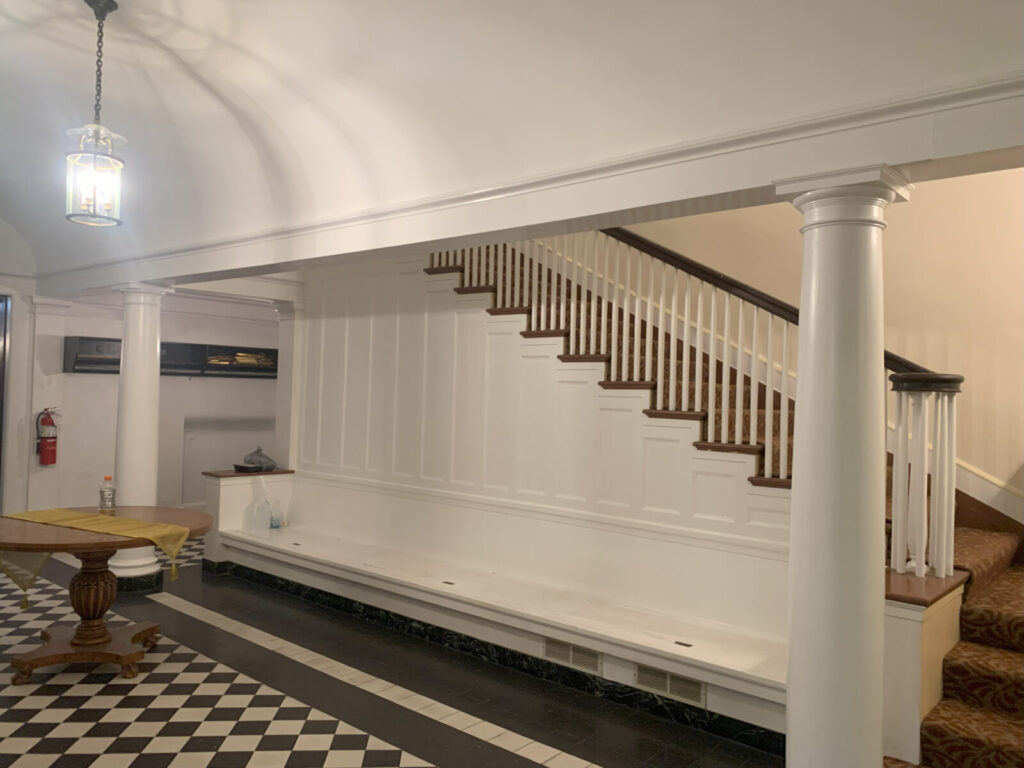 A white staircase with wood railings, white columns, and a checkered tile floor in a well-lit interior space.