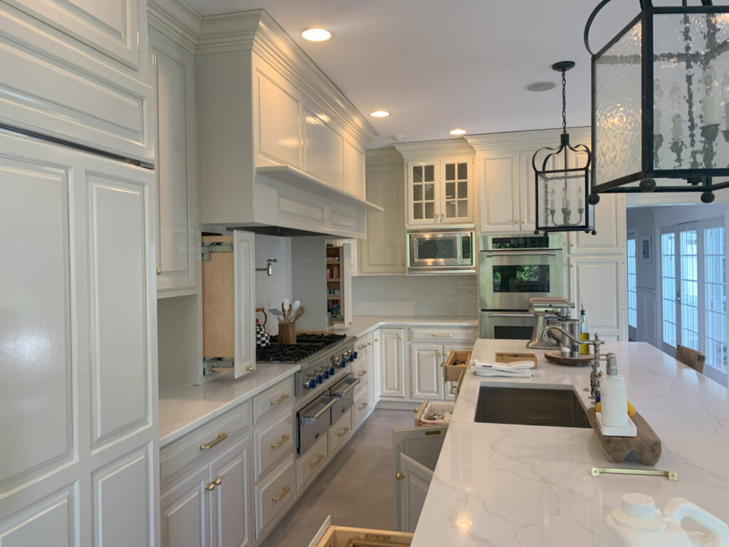 Modern kitchen with white cabinets, marble countertops, built-in appliances, and a large island with a sink and faucet.