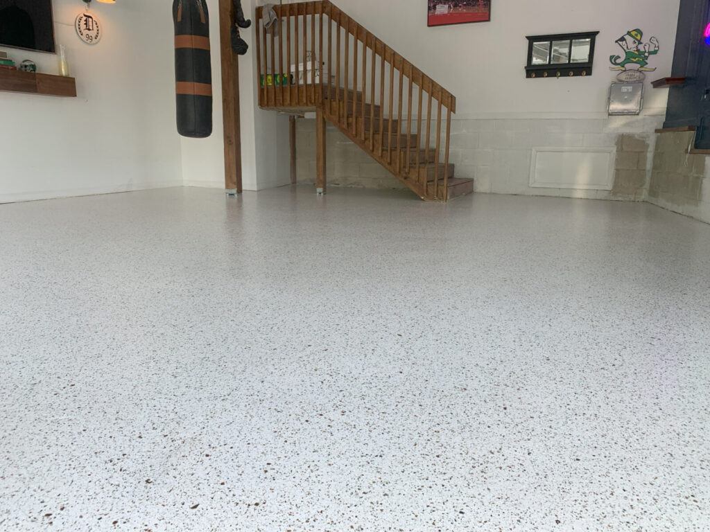 A clean garage with a speckled epoxy floor, wooden stairs, a punching bag, and various wall decorations.