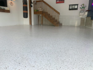 A clean garage with a speckled epoxy floor, wooden stairs, a punching bag, and various wall decorations.