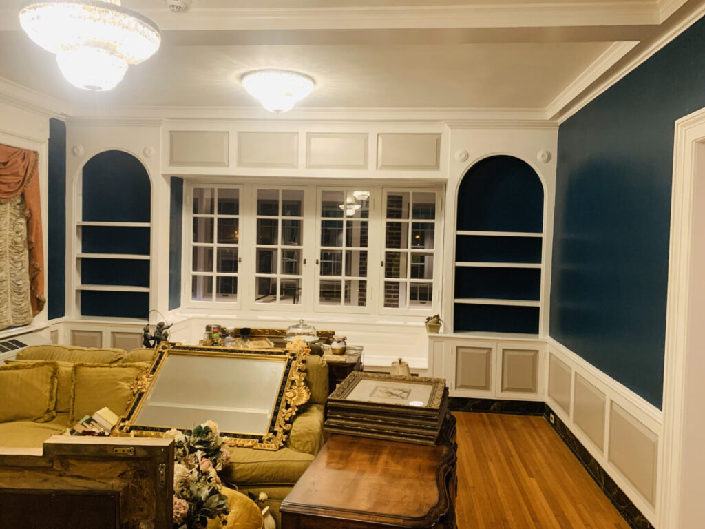 A well-lit living room with blue built-in shelves, wood floors, and furniture gathered in the center of the room.
