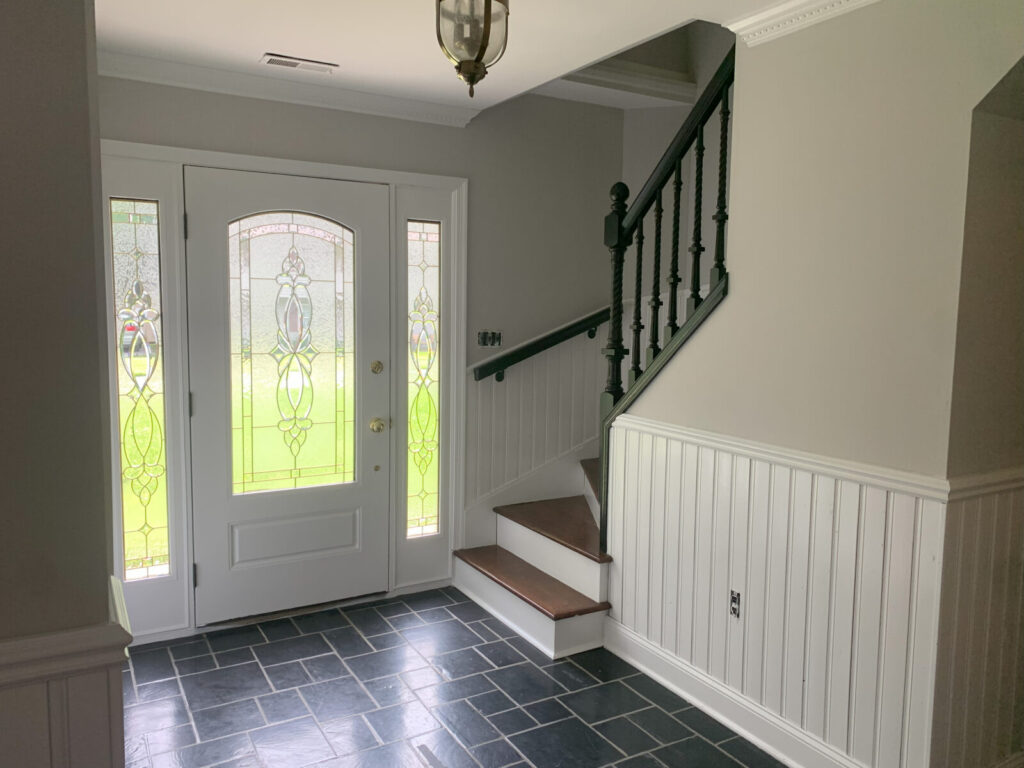 Bright entryway with a white front door, glass panels, tiled floor, and staircase with dark railing.